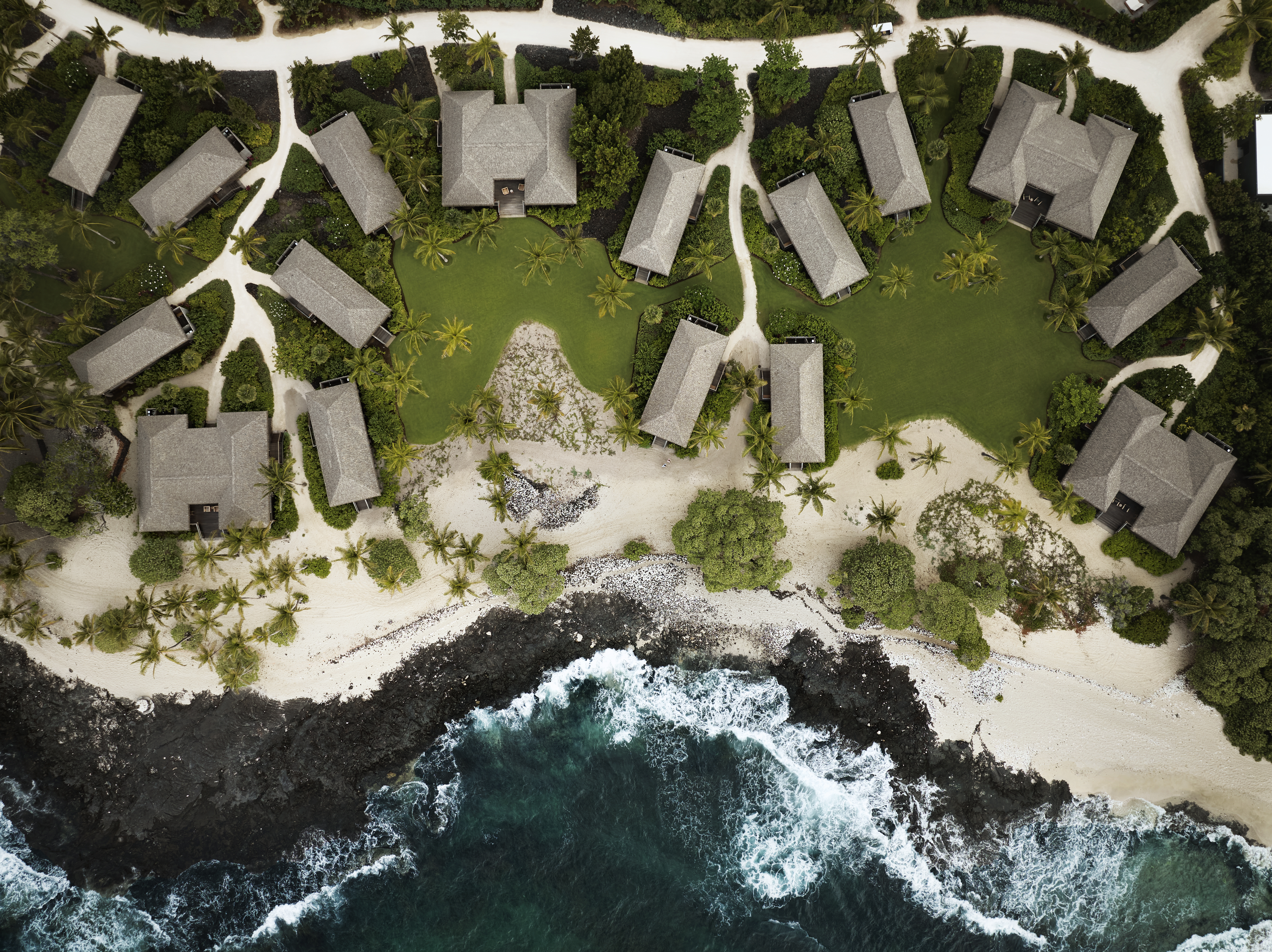Aerial view of beachfront villas surrounded by palm trees and green lawns.