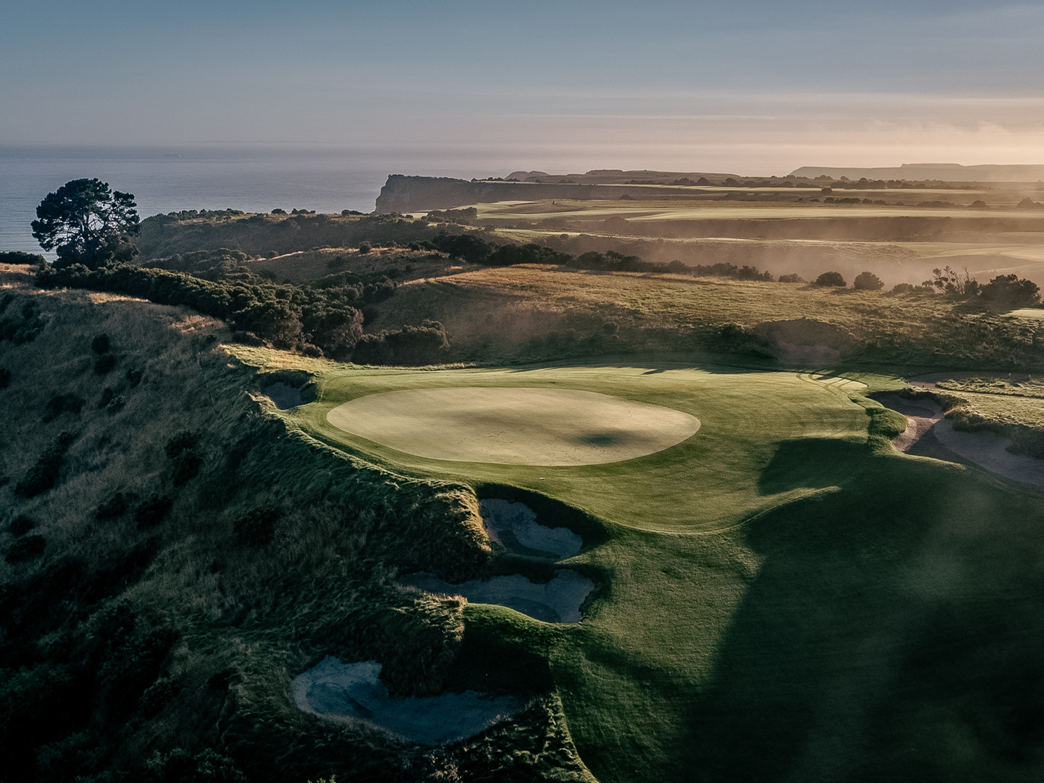 Clifftop golf course overlooking ocean with soft morning light.